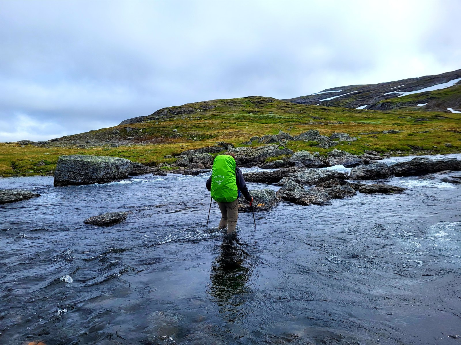 Simon mit grünem Rucksack und Wanderstöcken in einer Wasserfurt